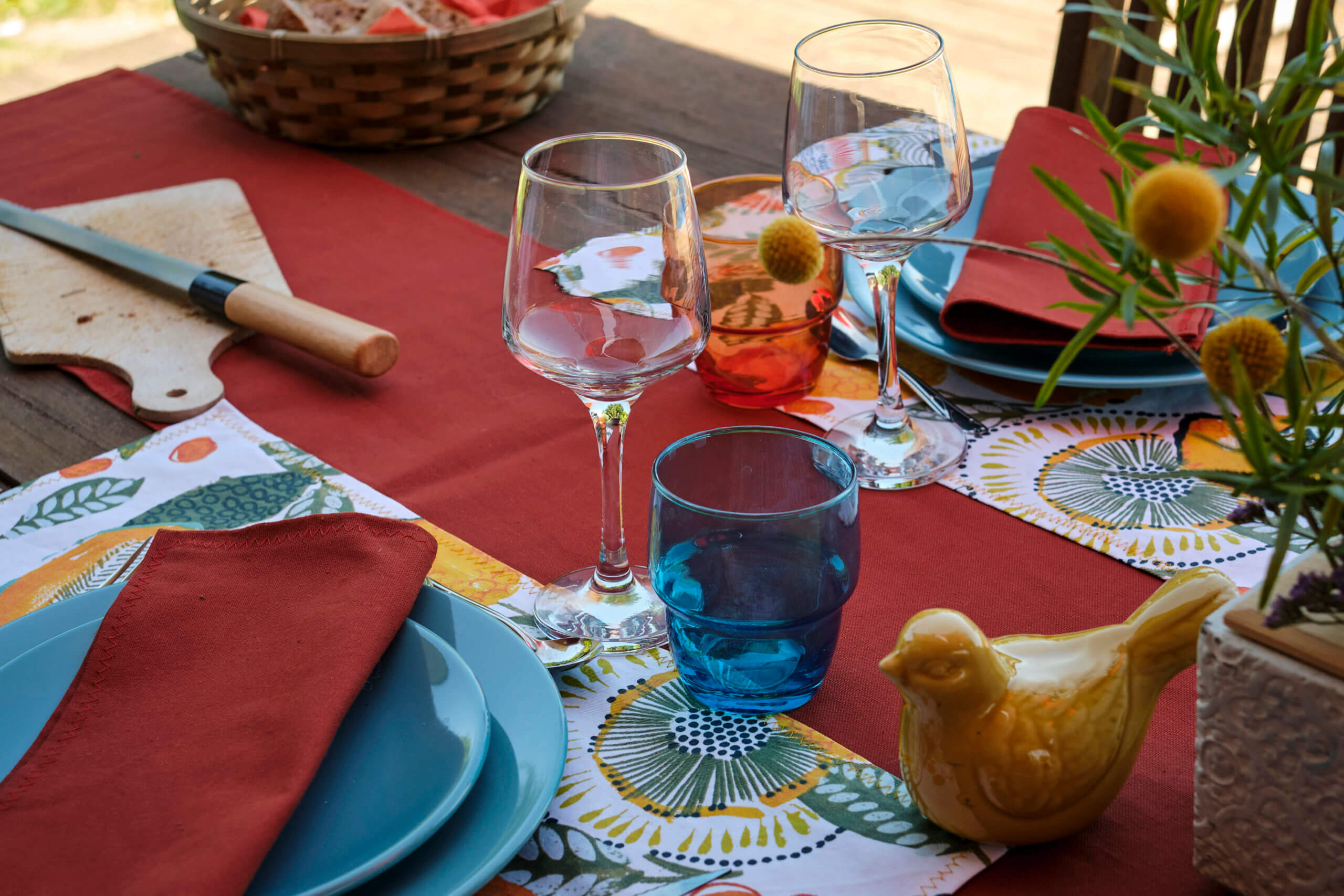 Décoration de table par Georgette MagritteS : chemin de table rouge, assiettes bleues, verres à vin, dessous de plats colorés, planche à pain, chardons, etc.