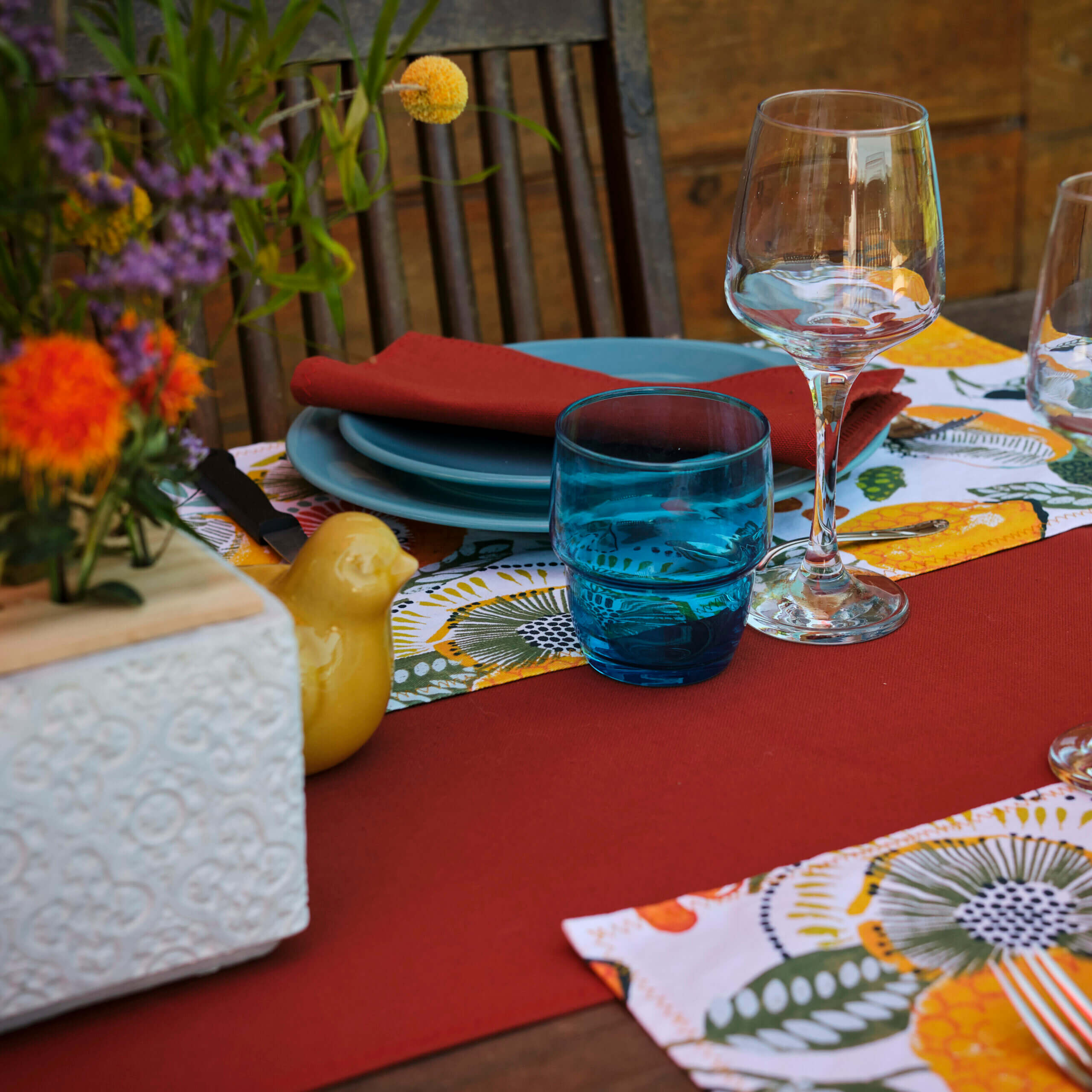 Table extérieure décorée par Georgette MagritteS. Chemin de table rouge, assiettes et verres bleus, serviettes rouges, fleurs. #wawwlatable